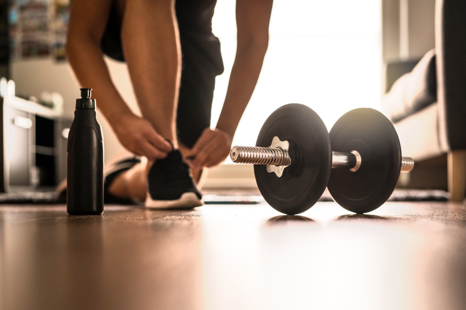 Morning workout routine in home gym. Fitness motivation and muscle training concept. Man in sneakers tying shoelaces in sunlight. Athlete starting exercise.